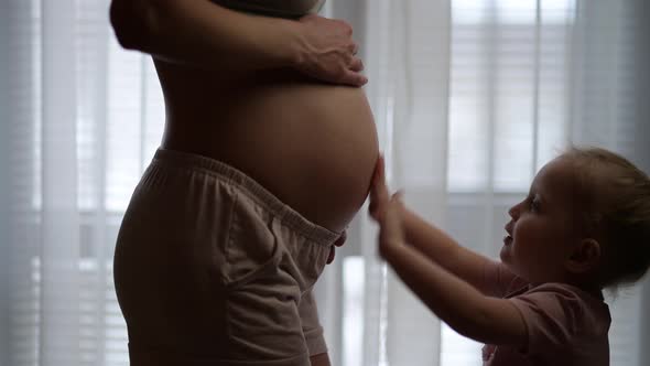 Little girl kissing her young mom's pregnant belly