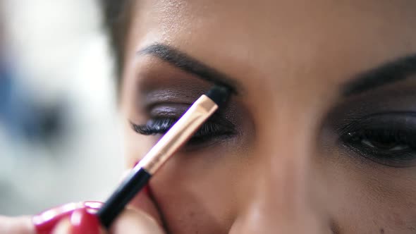 Closeup View of the Makeup Artist's Hands Using Brush to Paint Eyebrows for a Model with False