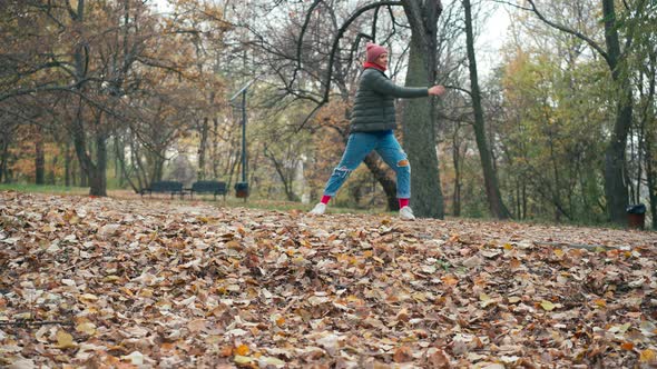 A Young Woman Is Having Fun and Jumping on Dry Autumn Leaves in the Park