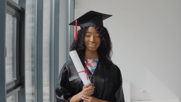 Young African American Female Graduate Standing in Front of the Camera with a Diplomas in Her Hands