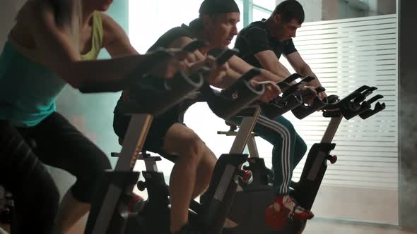 Sportmen Training Muscles of the Legs on Exercise Bicycles in Gym in a Row