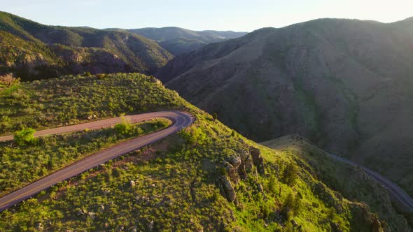 Aerial Shot Flying Over Winding Mountain Road Revealing Shadowy Dark Mountain Valley During Sunset N