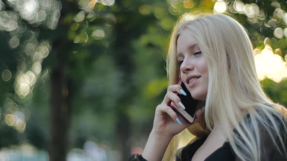 Cute Blonde Caucasian Pretty Girl with Long Hair Smiling Talking on Cell Phone in Park and Hanging