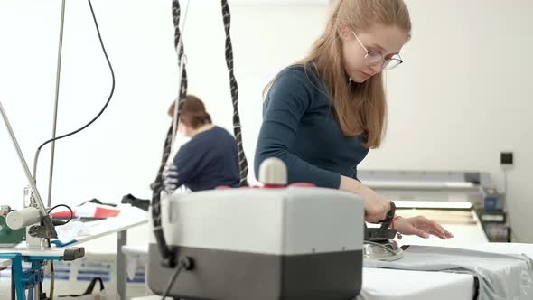 employee of a clothing factory smoothes her sewn clothes with a steam iron