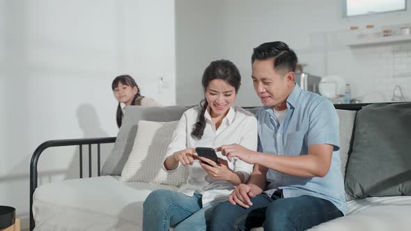 Asian family kid, mother, father playing game on smartphone together in living room at home