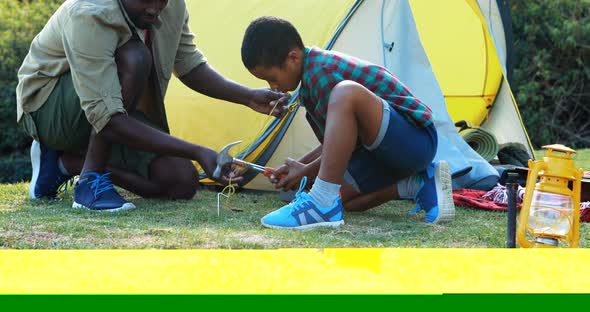 Father teaching son to use a hammer for setting up a tent