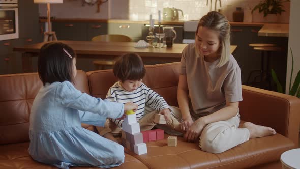 Young Asian Mother and Little Siblings Spend Time at Modern Flat Play Together Seated on Sofa Enjoy