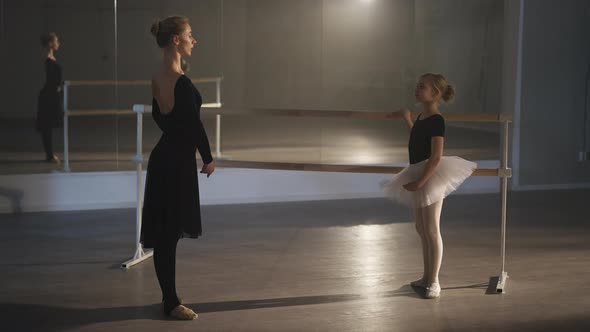 Side View Wide Shot of Slim Woman and Inspired Girl Rehearsing Eleve at Barre in Ballet Studio