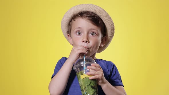 Cute boy Drinking Mojito cocktail From Plastic Cup Over Yellow Studio Background
