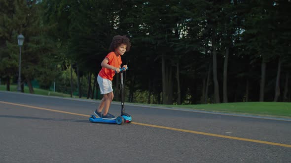 Excited Little Mixed Race Boy Riding Push Scooter