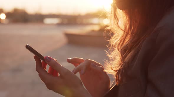 Young attractive business woman sitting outdoor on the bench and using smartphone.