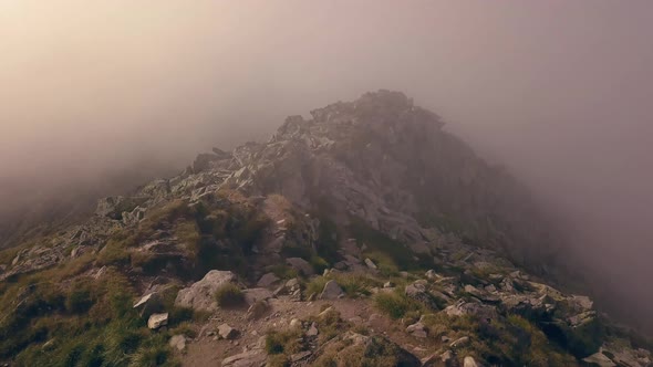 Flying over the top of a dirt pathway through the clouds leading to the summit of the mountain.