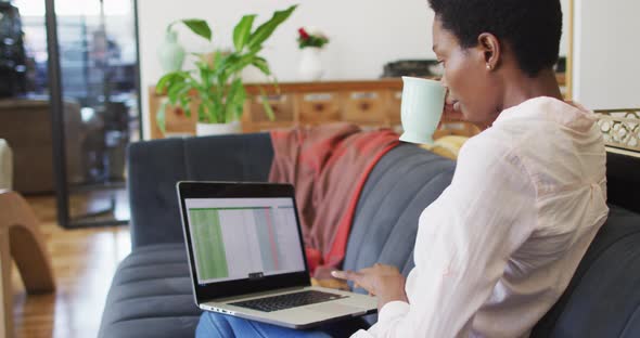 Happy african american woman sitting on sofa in living room, using laptop