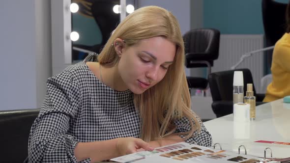 Young Woman Choosing New Hairstyle From Catalogue at Hairdresser Salon