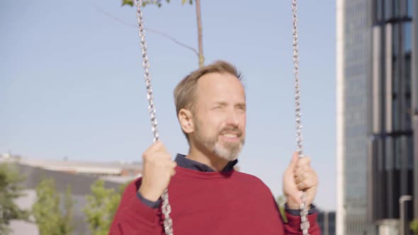 A Middleaged Handsome Caucasian Man Swings on a Swing with a Smile in an Urban Area