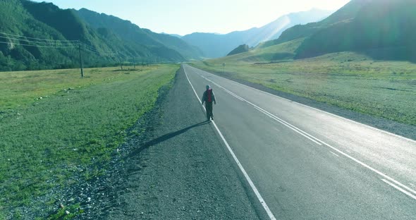Flight Over Hitchhiker Tourist Walking on Asphalt Road. Huge Rural Valley at Summer Day. Backpack alt