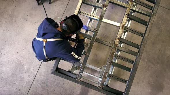 A man with a welding mask on fusing the Frame for a trailer.