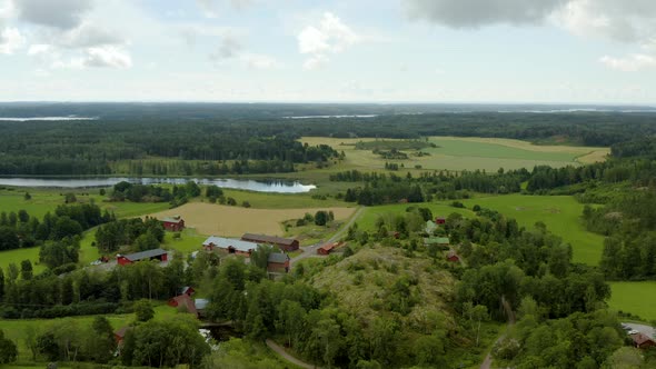 Aerial view around houses and buildings at a farm, on the countryside, partly sunny, summer day, in