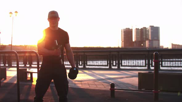 Young Sportive Man Training His Hands with Dumbbells on Sunset