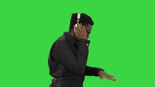 Young African American Man Listening To Music in Headphones and Grooving While Walking on a Green