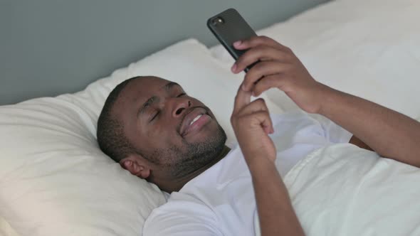 Smartphone Use By African Man Laying in Bed 