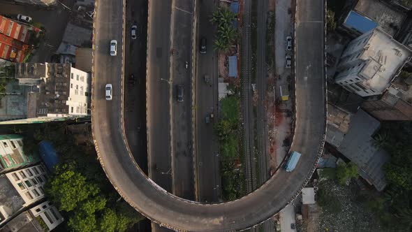 Aerial u-loop flyover over highway with cars and city buildings, drone ascending top shot view