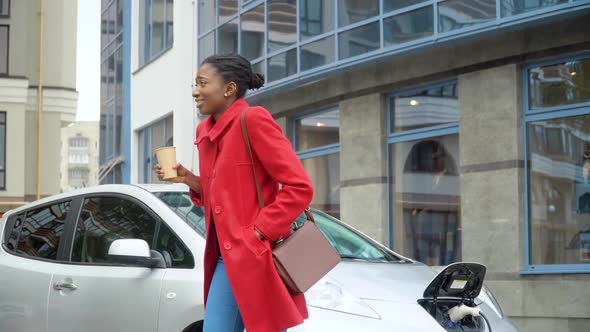 African American Girl Drinking Coffee Near Her Electric Car