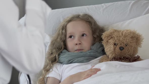 Cute Blond Child Lying in Bed while Doctor Examining Her