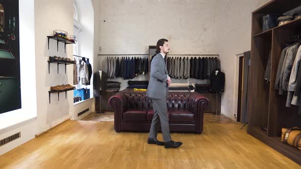 Young gentleman trying on grey suit in luxurious classy boutique shop.