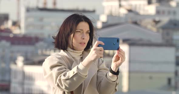 Close-up of Brunette Caucasian Woman with Brown Eyes Standing on City Street and Taking Photos