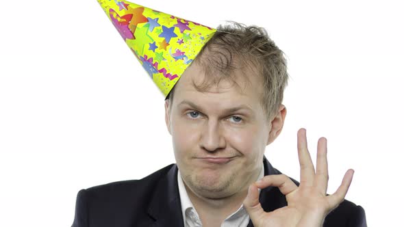 Drunk Sleepy Young Businessman with Hangover in Festive Cap Showing OK Sign