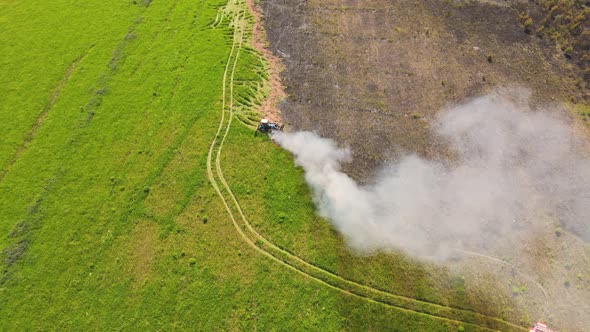 At the Edge of a Field Fire a Tractor Extinguishes the Fire