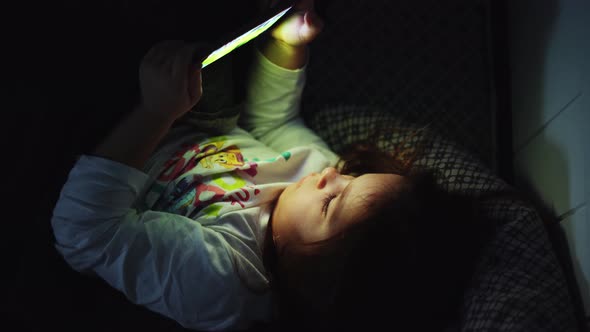 Baby Girl is Watching Video on Smartphone in Bed Before Sleeping at Evening