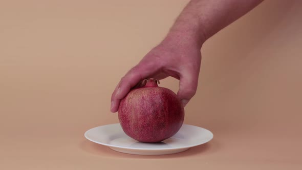 Closeup Male Hands Lay and Turn a Red Pomegranate on a White Plate