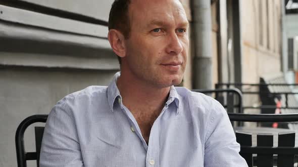 Adult Handsome European Man with Gray Eyes in a Blue Shirt Drinks a Hot Drink in a Summer Outdoor