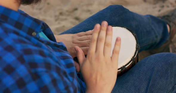 A Closeup of a Man Playing a Small Drum on the Beach