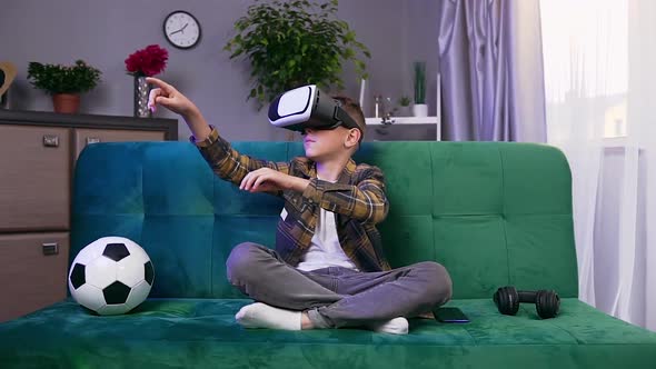 Boy Sitting on Comfortable Sofa in Living-Room and Playing on Imaginary Screen in Virtual Reality