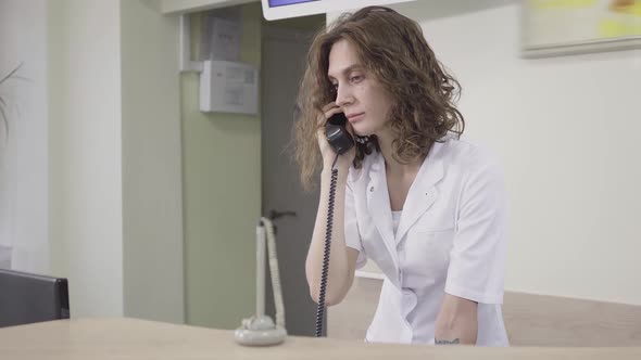 Receptionist Receiving Call in Hospital. Portrait of Concentrated Caucasian Woman Consulting Patient