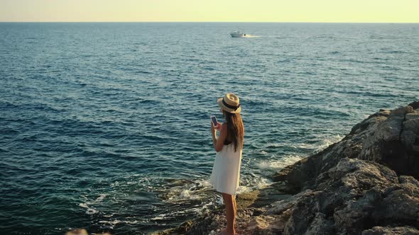 Woman is Taking Photo of Sea Water By Smartphone Standing on Rock Shore