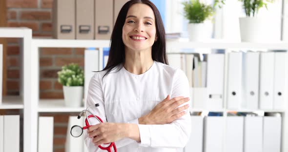 Smiling Female Doctor in White Coat is Holding Stethoscope