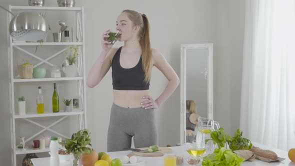 Pretty Slender Woman Drinking Green Herbal Cocktail and Smiling at Camera