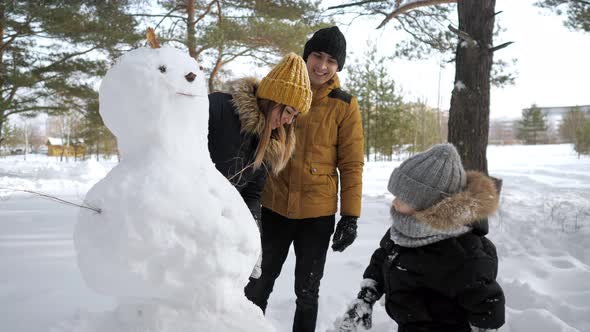 Happy Family Mom Dad and Son are Making a Snowman in Winter City Park