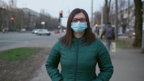 A Young Girl in Glasses and Medical Mask Stands on the Street