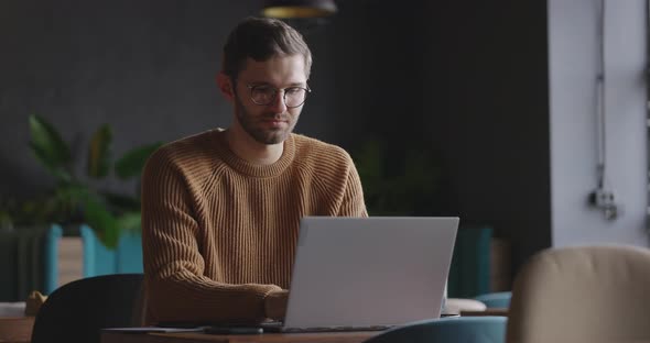 Adult Man Sits in Cafe in Daytime and Using the Laptop for the Remote Work