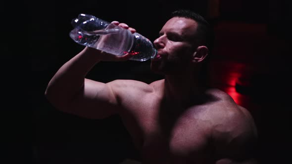 Tough Shirtless Man Drinking Water From the Bottle in the Dark