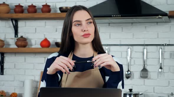 Thoughtful woman housewife in apron thinks solution problem in home kitchen