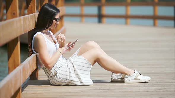 Cute Woman Is Reading Text Message on Mobile Phone While Sitting in the Park.