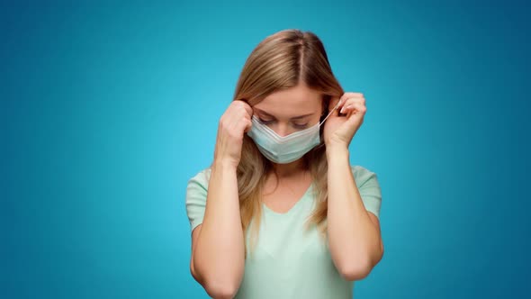 Young Woman Takes Off Medical Mask and Smiles Against Blue Background