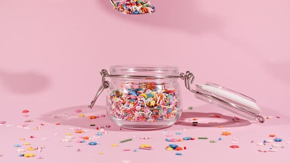 Colorful Candy Confectionery Run Poured Into a Jar Glass on Pink Background