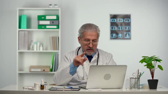 Professional Male Doctor in White Medical Coat Making Conference Call on Laptop Computer Consulting